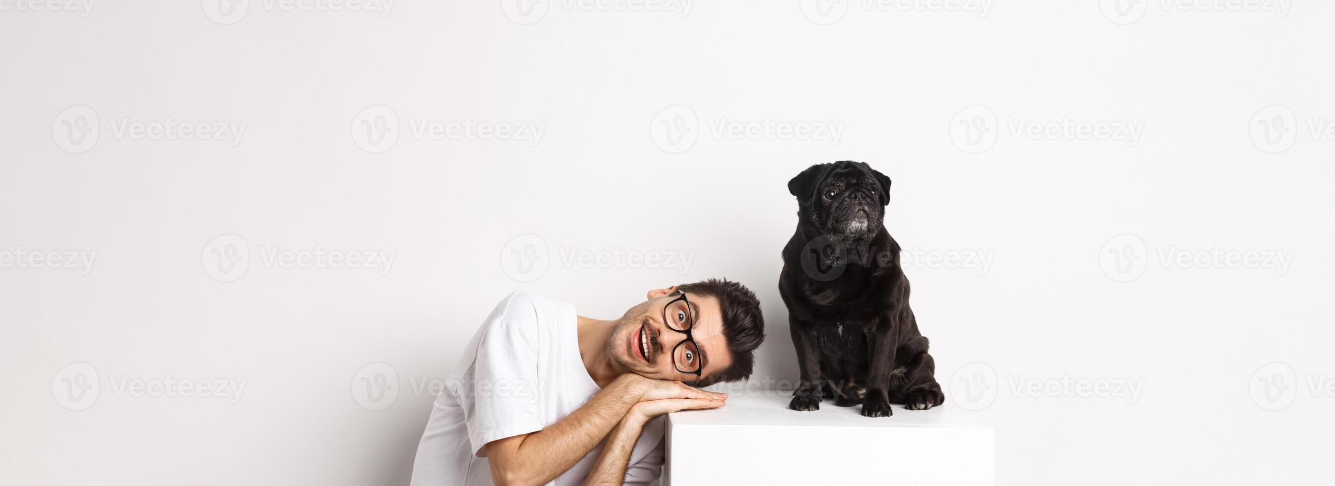 Handsome young man lay head near cute black dog, smiling and looking at camera, white background photo