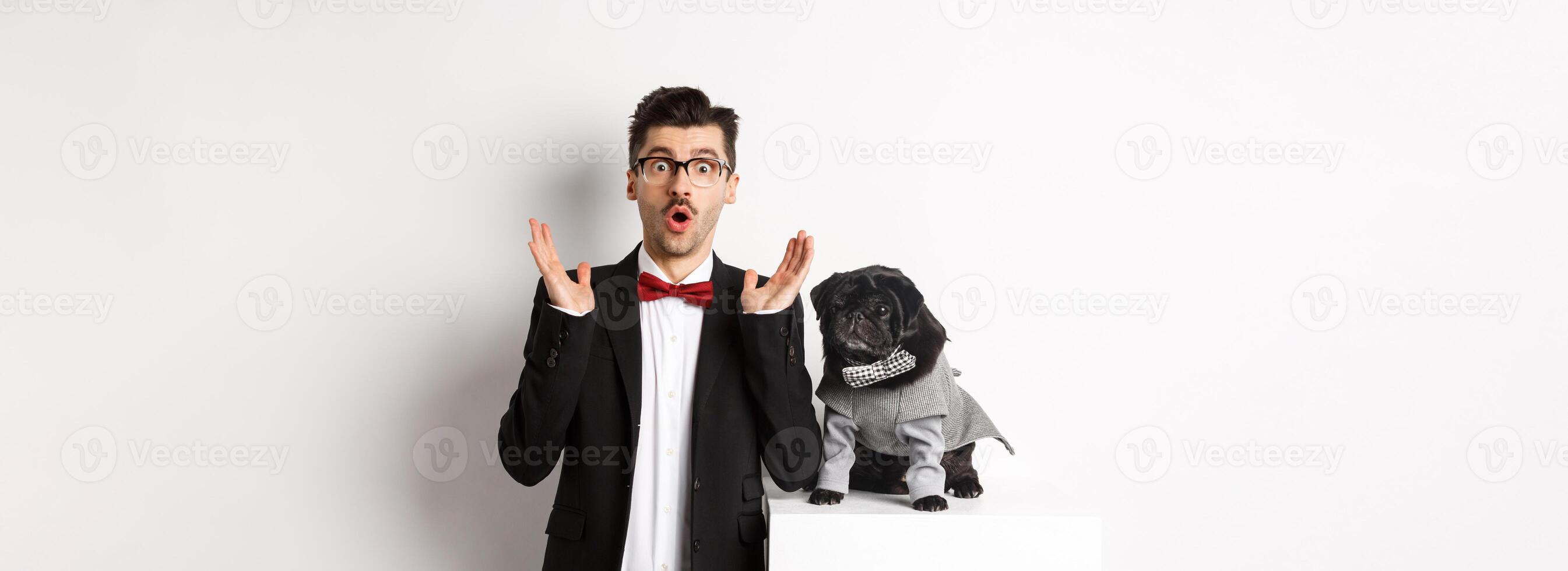 Animals, party and celebration concept. Image of dog owner and cute pug in costumes suits staring surprised at camera, reacting on promo offer, white background photo