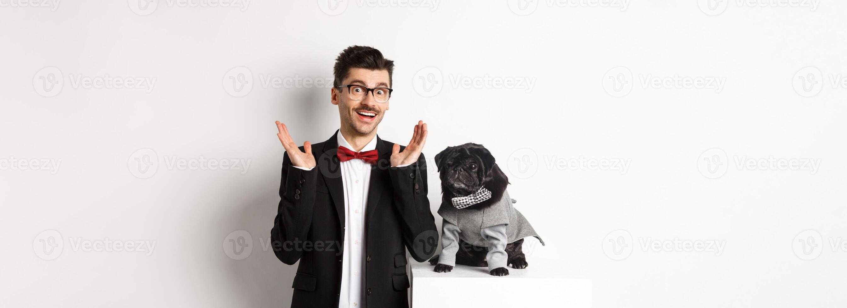 Animals, party and celebration concept. Handsome man and cute dog in costumes suits staring surprised at camera, reacting on promo offer amazed, white background photo