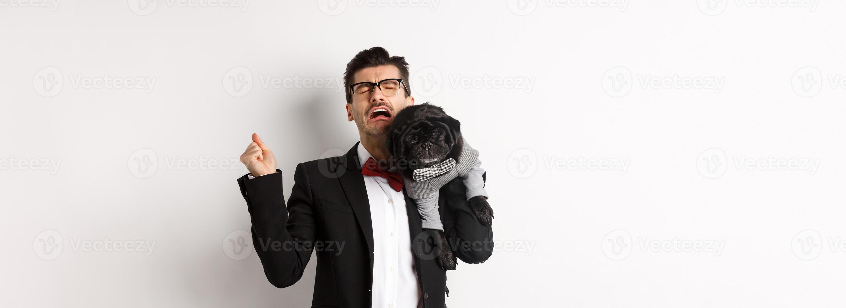 Sad man in suit, holding cute small dog on shoulder and crying with disappointed face, standing distressed over white background photo