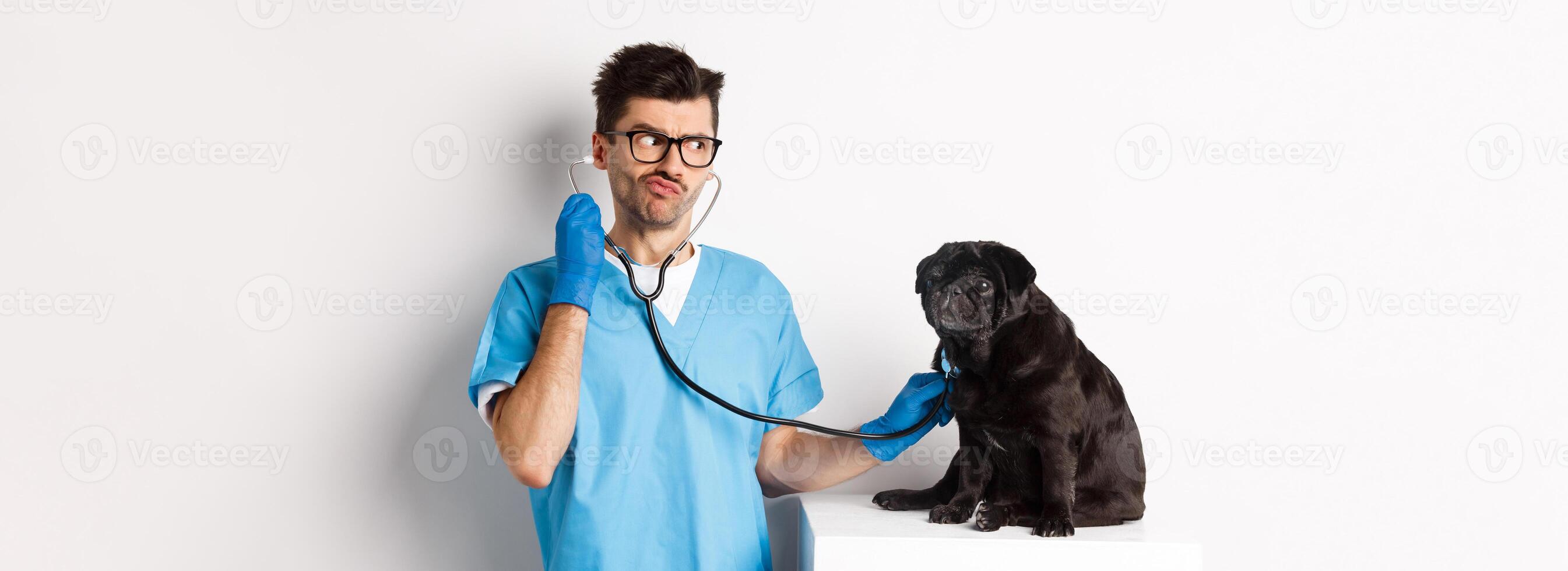 Confused male doctor veterinarian checking dog with stethoscope, looking puzzled, standing over white background photo