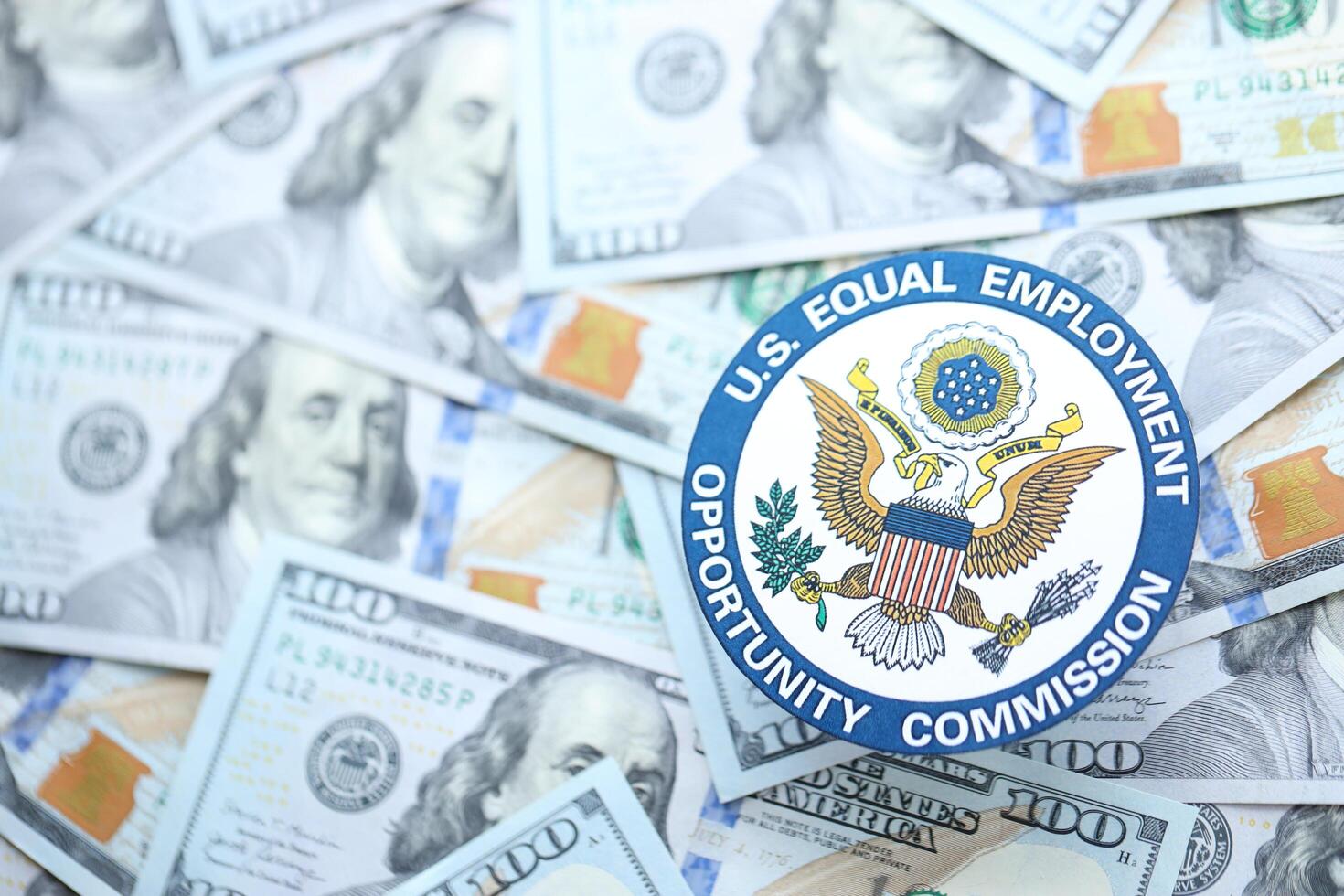 KYIV, UKRAINE - JUNE 26, 2024 U.S. Equal Employment Opportunity Commission coat of arms on big amount of US dollar banknotes photo