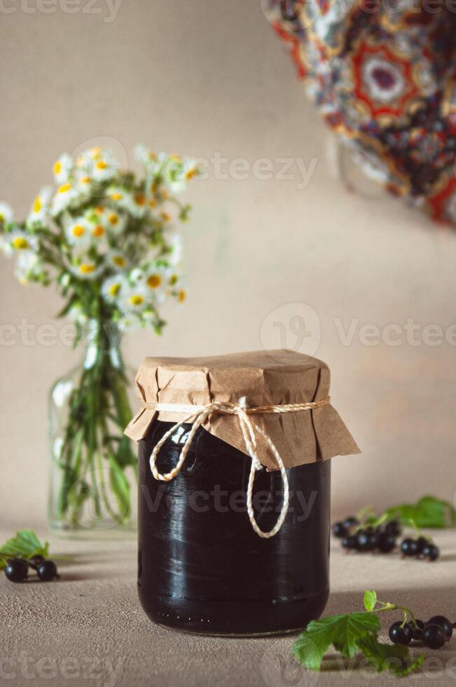 Black currant jam jar with fresh berries and leaves on background photo