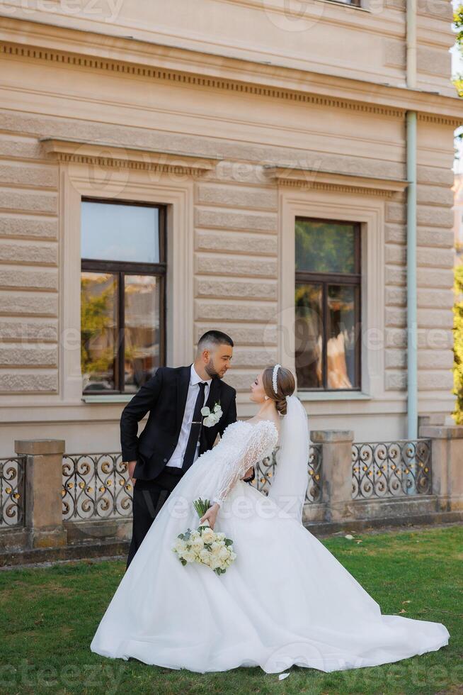 A bride and groom are posing for a picture in front of a building. The bride is wearing a white dress and the groom is wearing a suit. Scene is happy and celebratory, as the couple is getting married photo