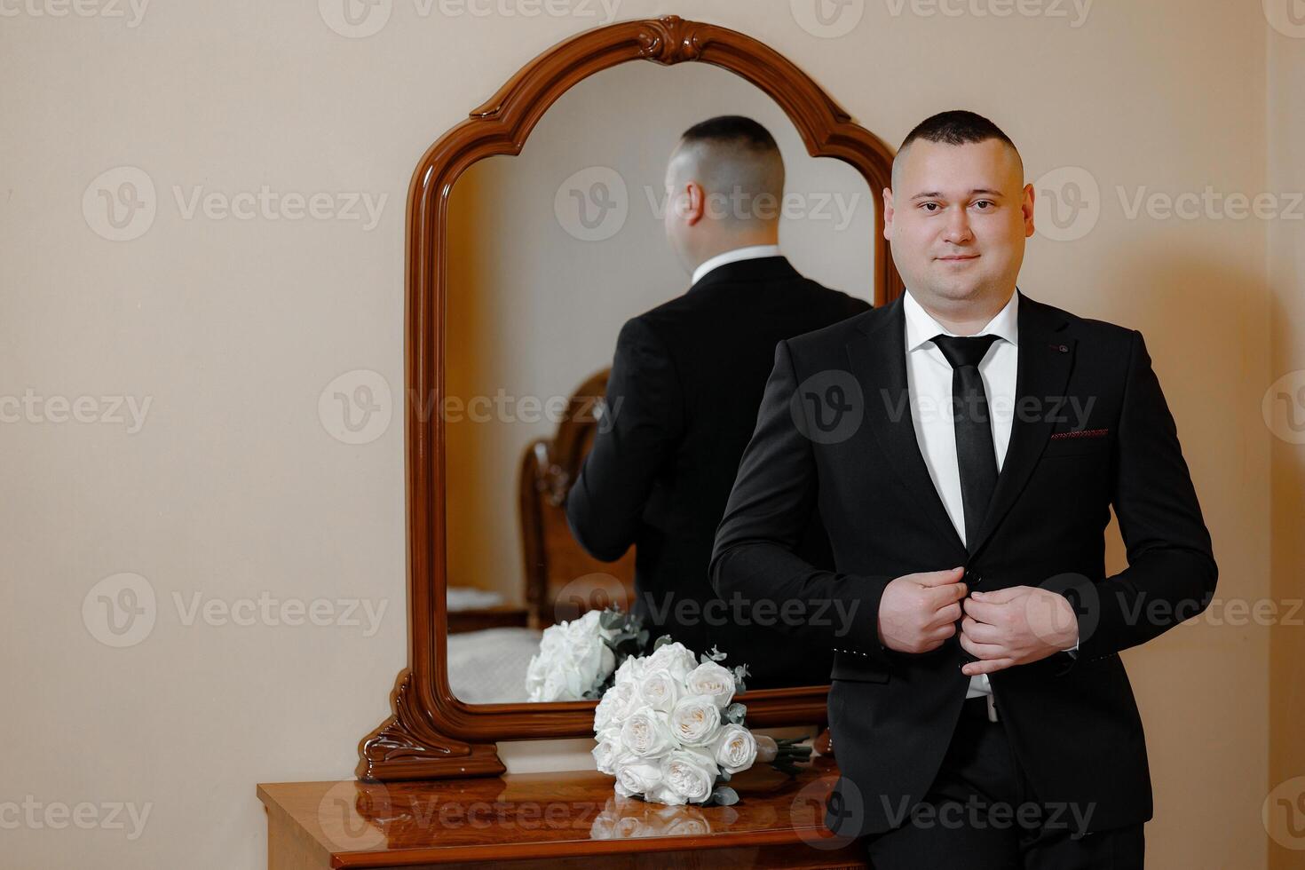 A man in a suit stands in front of a mirror, adjusting his tie. Concept of formality and elegance, as the man is dressed in a suit and tie, and the mirror reflects his appearance photo