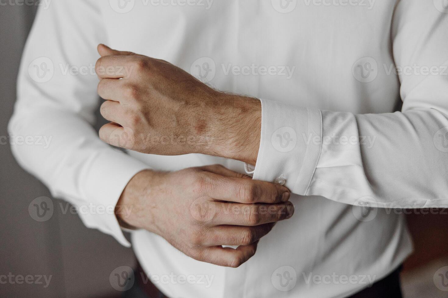 A man is wearing a white shirt and is adjusting his sleeve. Concept of formality and attention to detail, as the man is taking care to ensure his shirt is properly fitted and neat photo