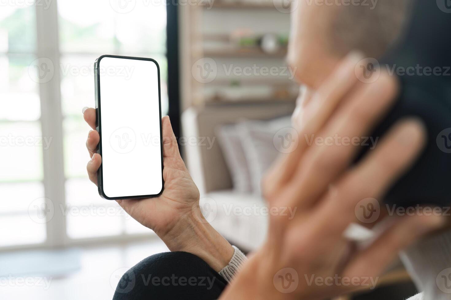 Man Holding Smartphone with Blank Screen While Sitting Indoors Near Window in Modern Home photo