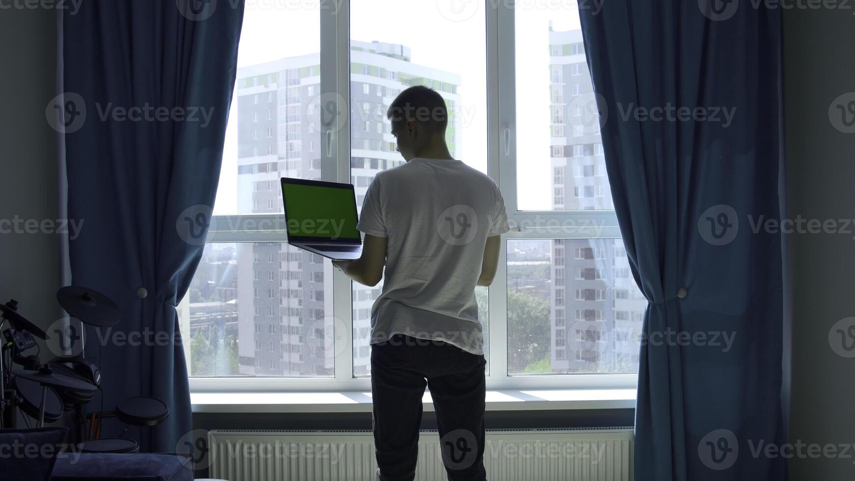 Back view of a young man in white t shirt working on laptop with green chroma key screen. Media. Concept of using modern technologies for remote work. photo