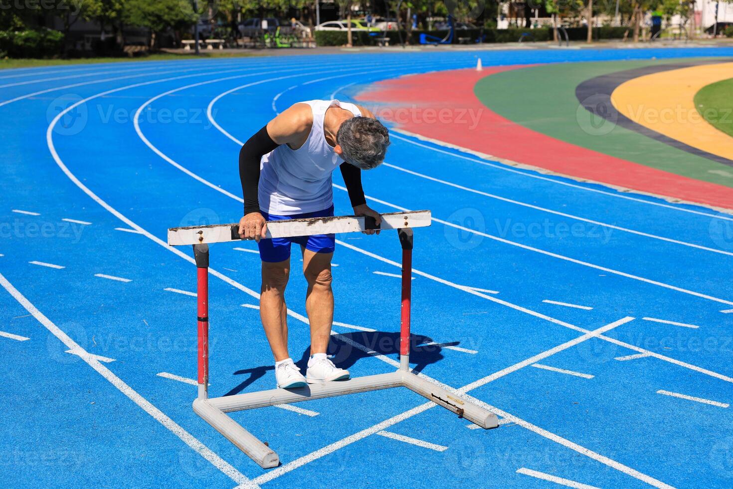 Senior Asian athlete is practicing hurdling running in the professional blue track for professional exercise, sport training workout and healthy for longevity concept photo