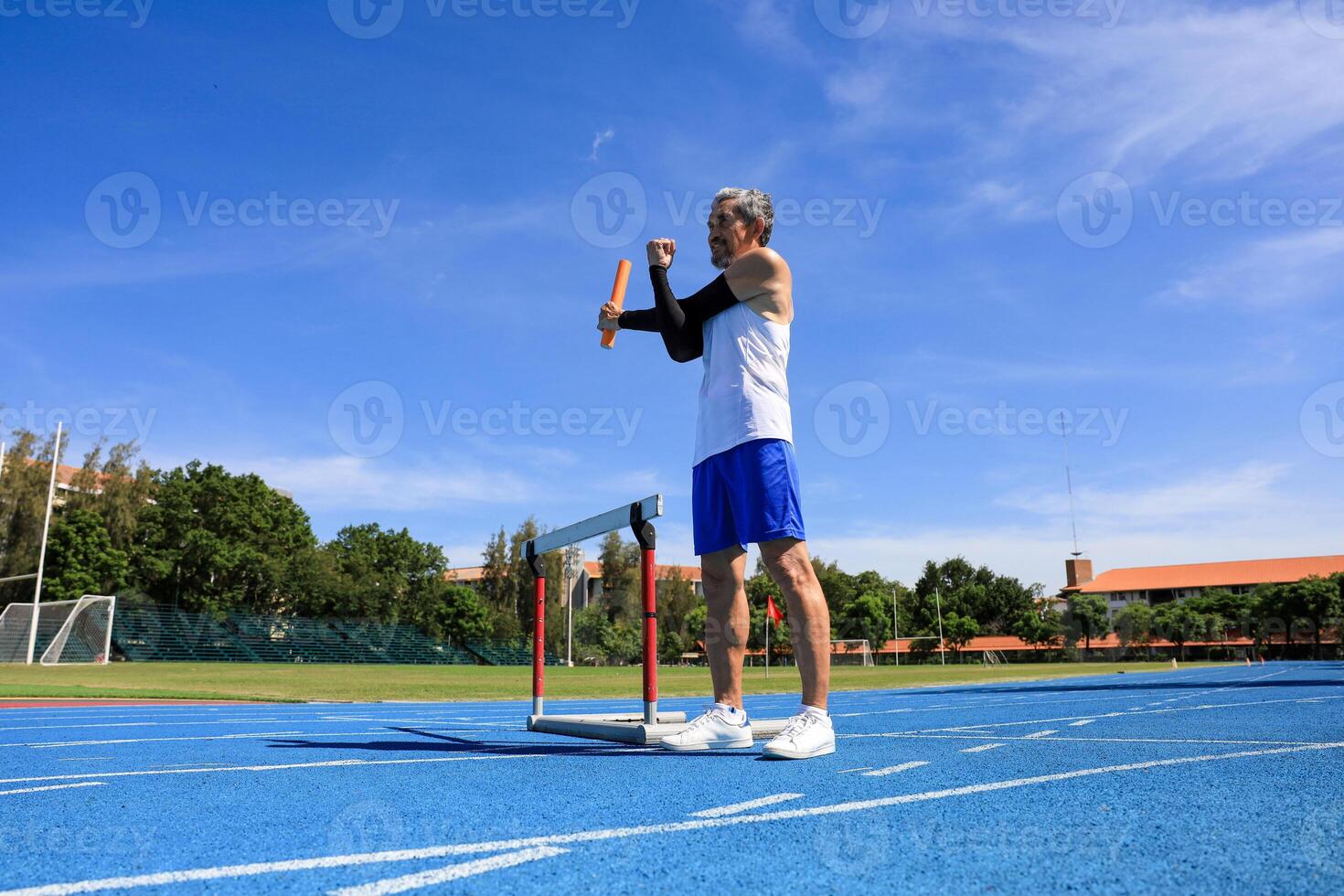 Senior Asian athlete is practicing hurdling running in the professional blue track for professional exercise, sport training workout and healthy for longevity concept photo
