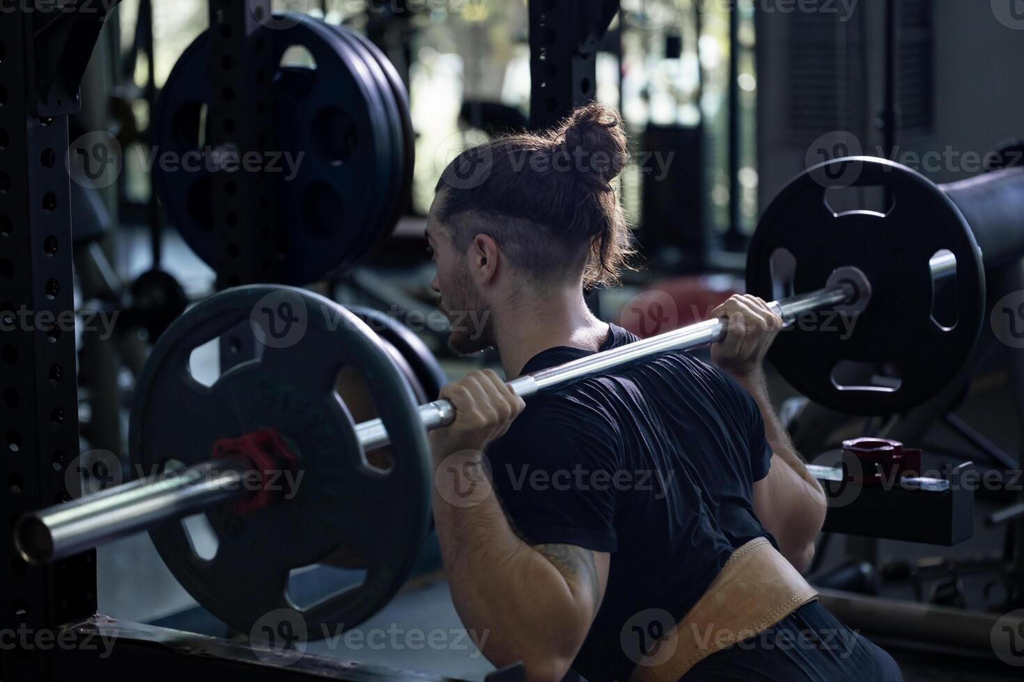 Caucasian muscular body builder sport man is practice weight training on squat barbell for core muscle inside gym with dark background for exercising and workout photo