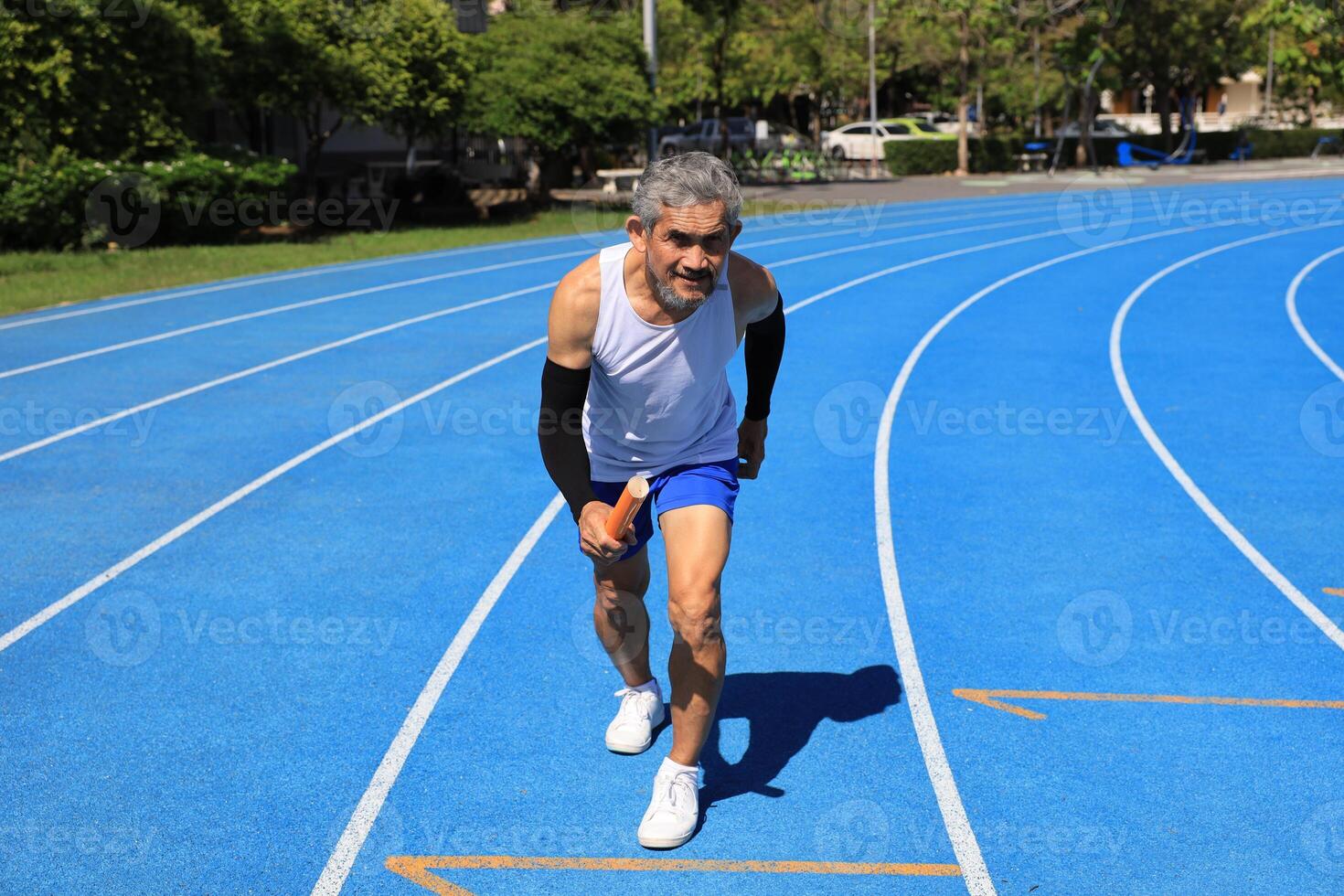 Senior Asian athlete is practicing running with relay baton in the professional blue track for professional exercise, sport training workout and healthy for longevity concept photo
