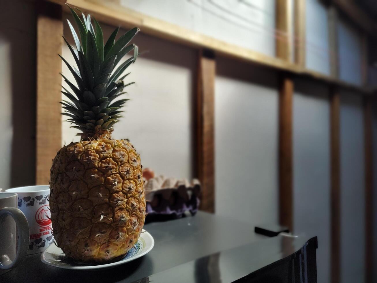 A pineapple sits on a plate next to a cup photo