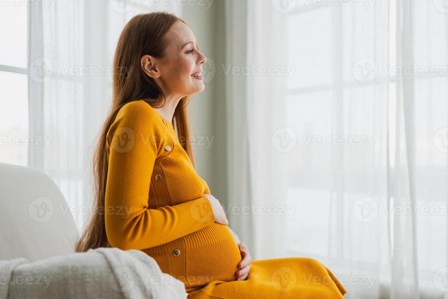 Pregnancy motherhood people expectation future. Pregnant woman with big belly sitting on chair near window at home. Girl hugging her tummy enjoying pregnancy. Maternity tenderness parenthood new life photo