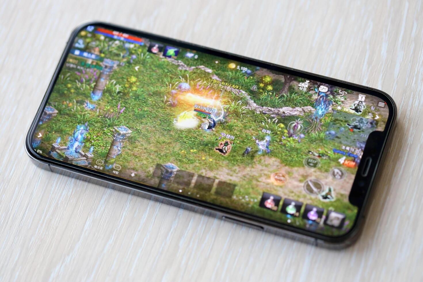 Lineage M mobile iOS game on iPhone 15 smartphone screen on wooden table during mobile gameplay photo