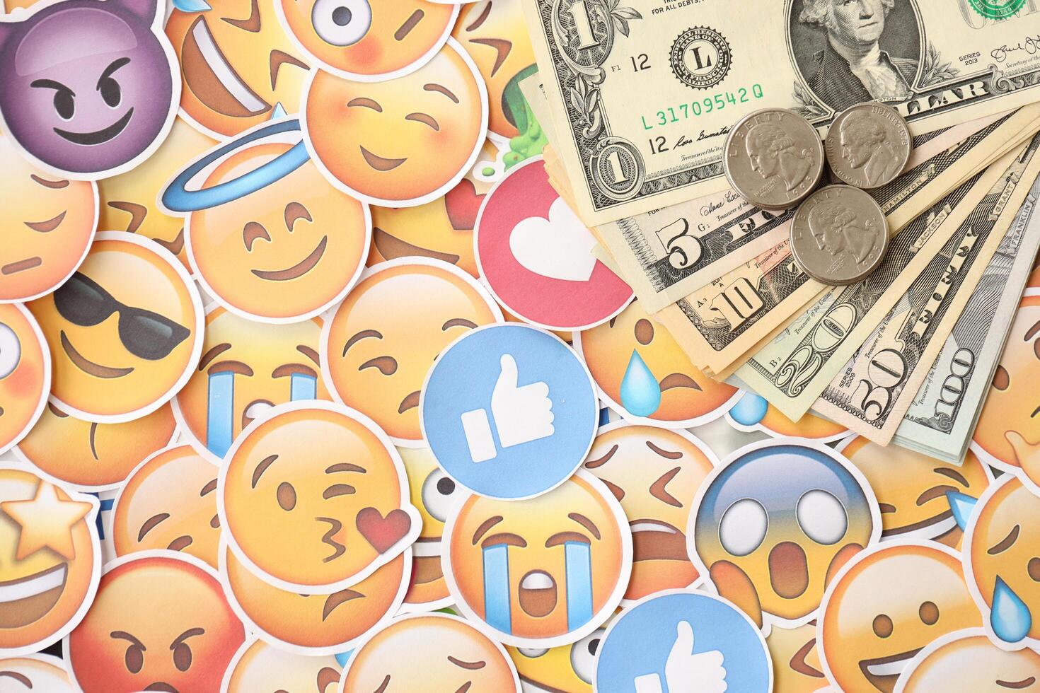 KYIV, UKRAINE - APRIL 20, 2024 USD dollars money and large set of stickers with Emoji yellow faces. The concept of smm, smo paid service for boost in social media photo