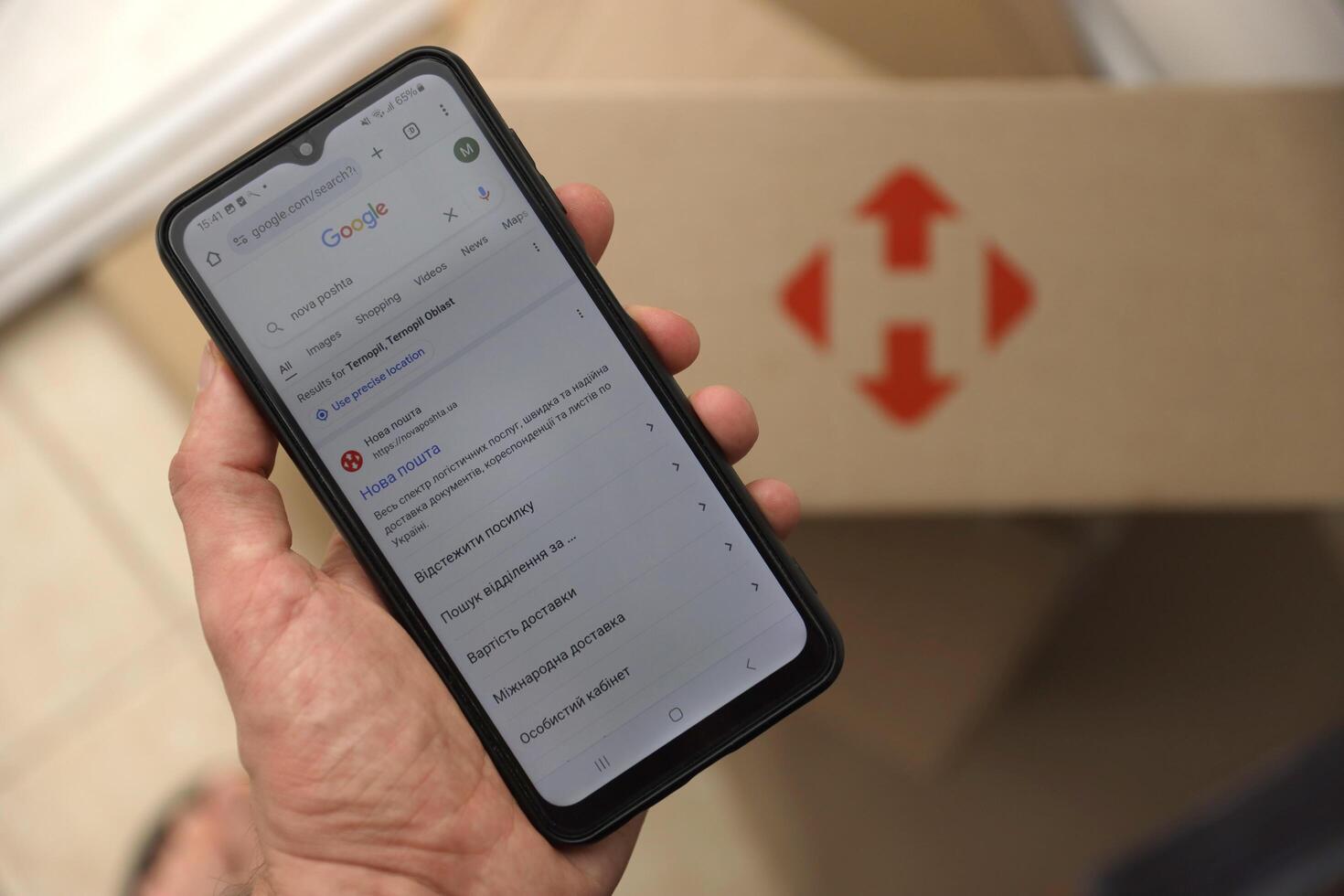 KYIV, UKRAINE - APRIL 20, 2024 Nova Poshta Logotype on cardboard box and website on smartphone screen. Nova Poshta is best ukrainian postal service company photo