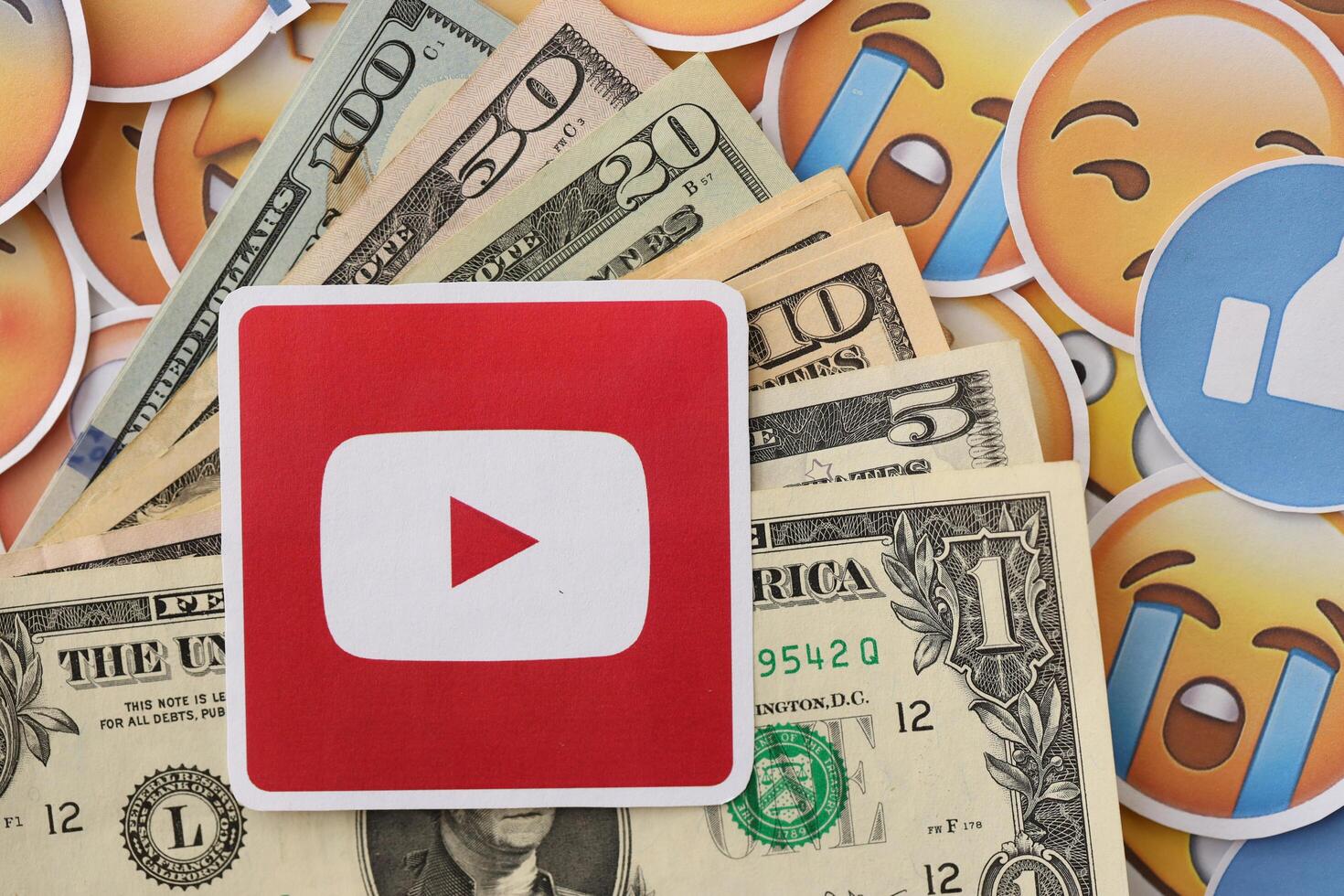 KYIV, UKRAINE - APRIL 20, 2024 YouTube logo and many usd money bills. Symbol of famous social network platform and dollar currency banknotes on lot of emoji reactions photo