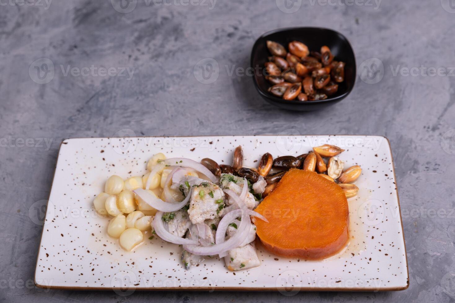 Tray of Ceviche next to a portion of corn, served on a grey background. photo