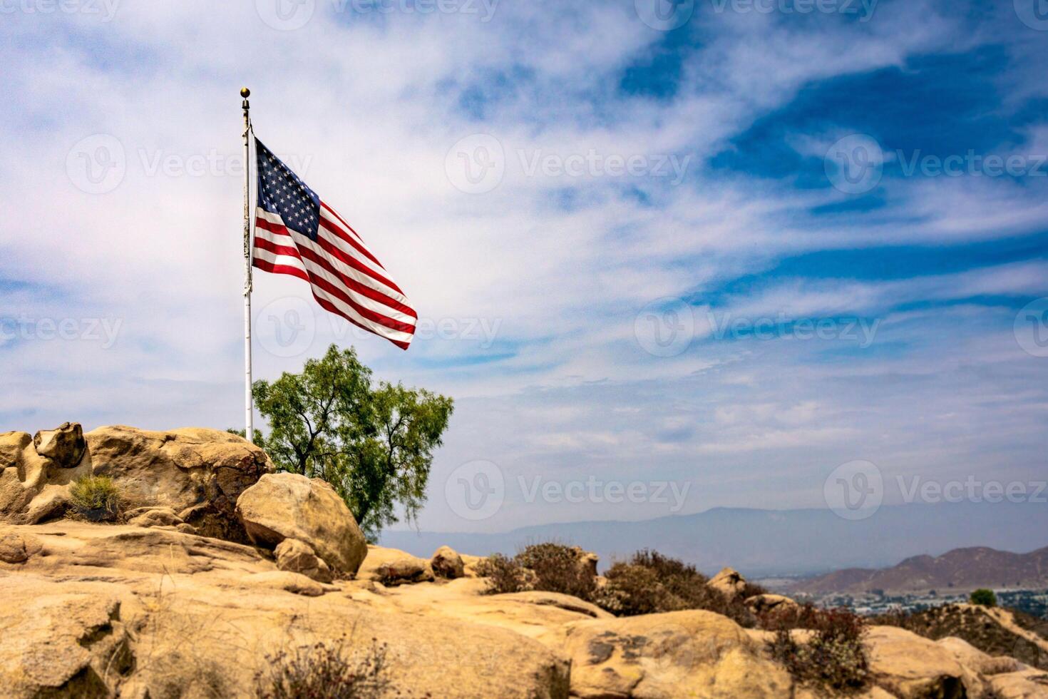 An american flag on a staff, waving in the wind with a clear blue sky and distant mountains as its backdrop, symbolizing usa independence day photo