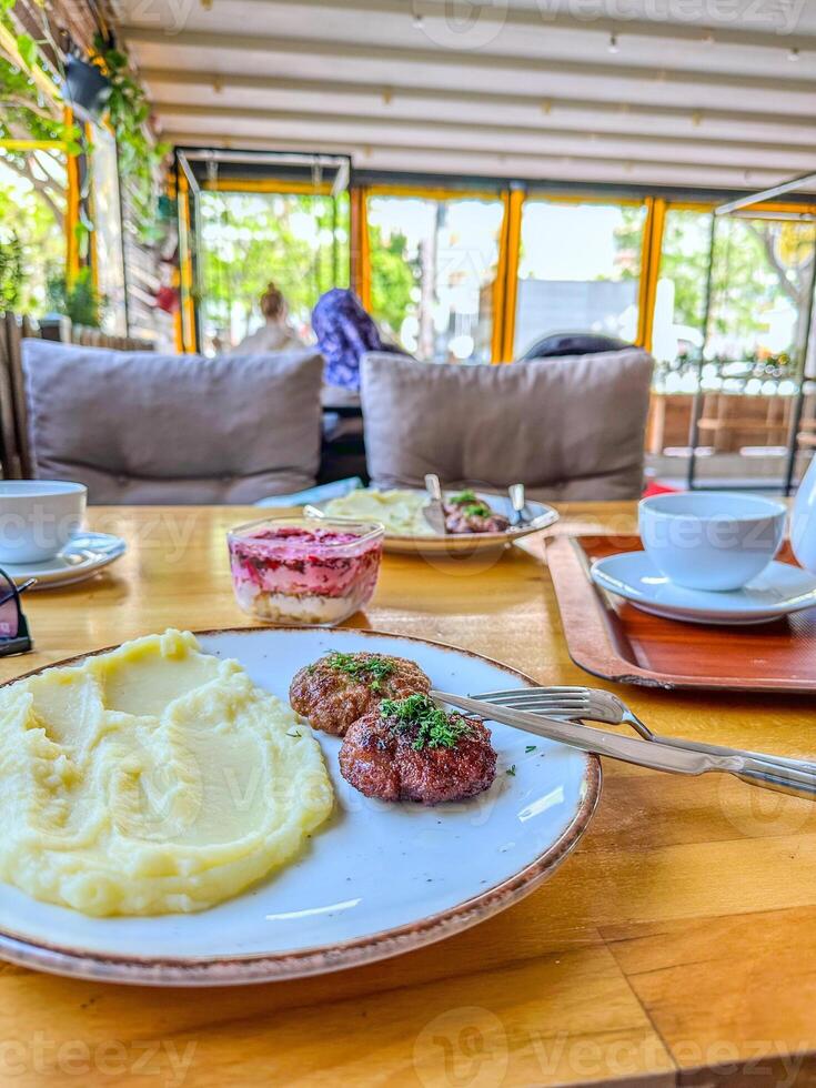 Lunch at the restaurant. A portion of beef patties in Russian style with mashed potatoes and herbs. In the background - salad with beetroot and herring, a cup of coffee and the interior of the cafe. photo