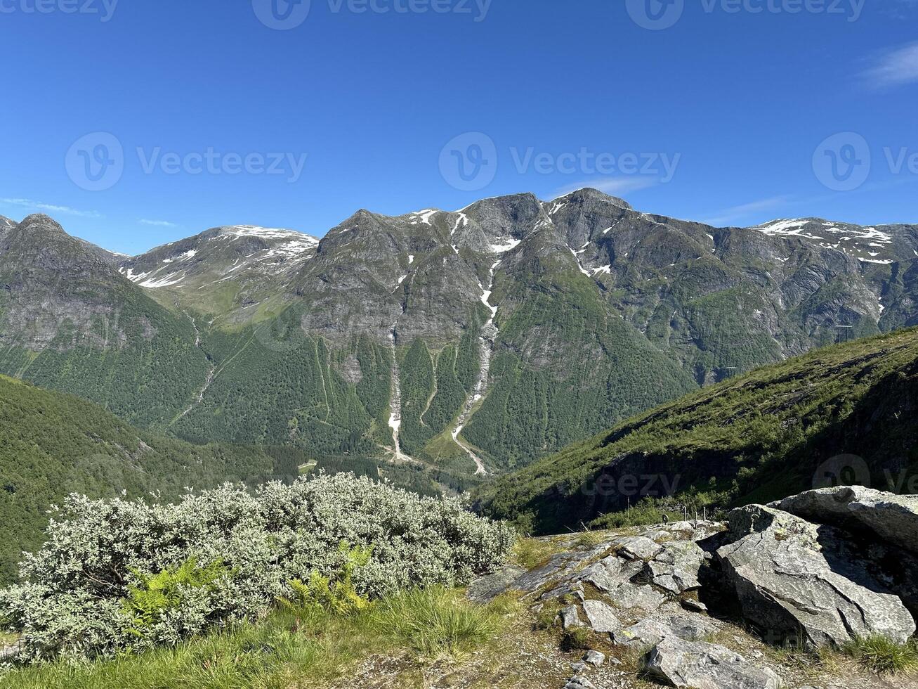 Mountain range with trees, rocks in foreground, blue sky in background photo
