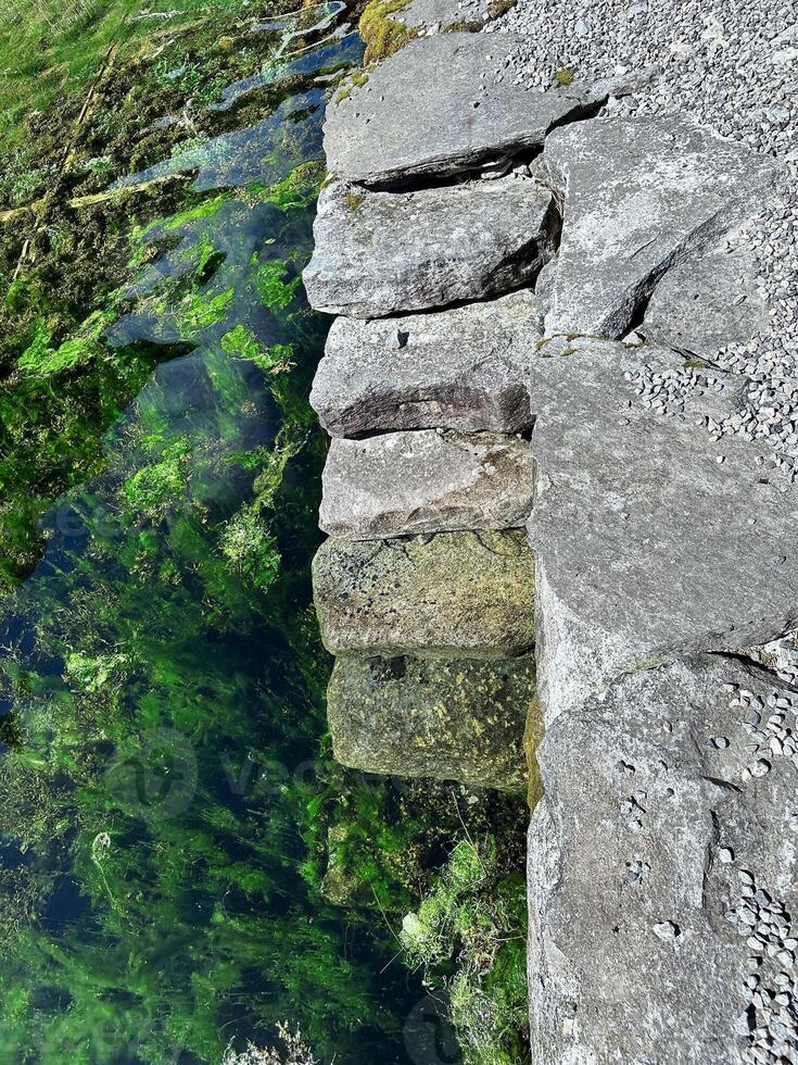 A staircase of stones going under the water of a crystal clear lake in the mountains of Norway, underwater flora in the form of bright algae is visible at the bottom photo