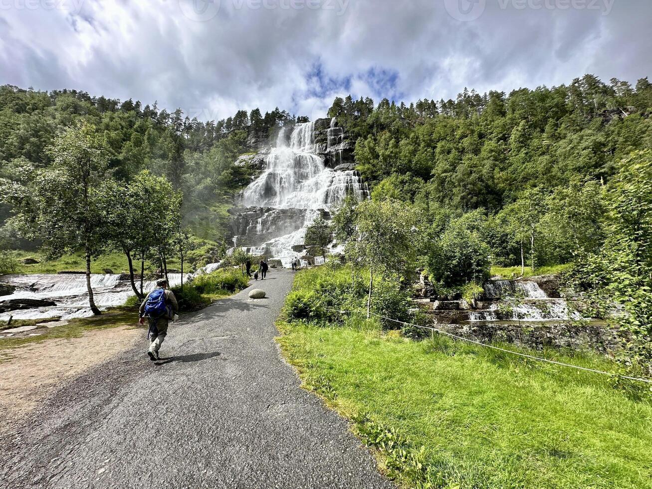 A person is strolling towards a waterfall located in a forest photo