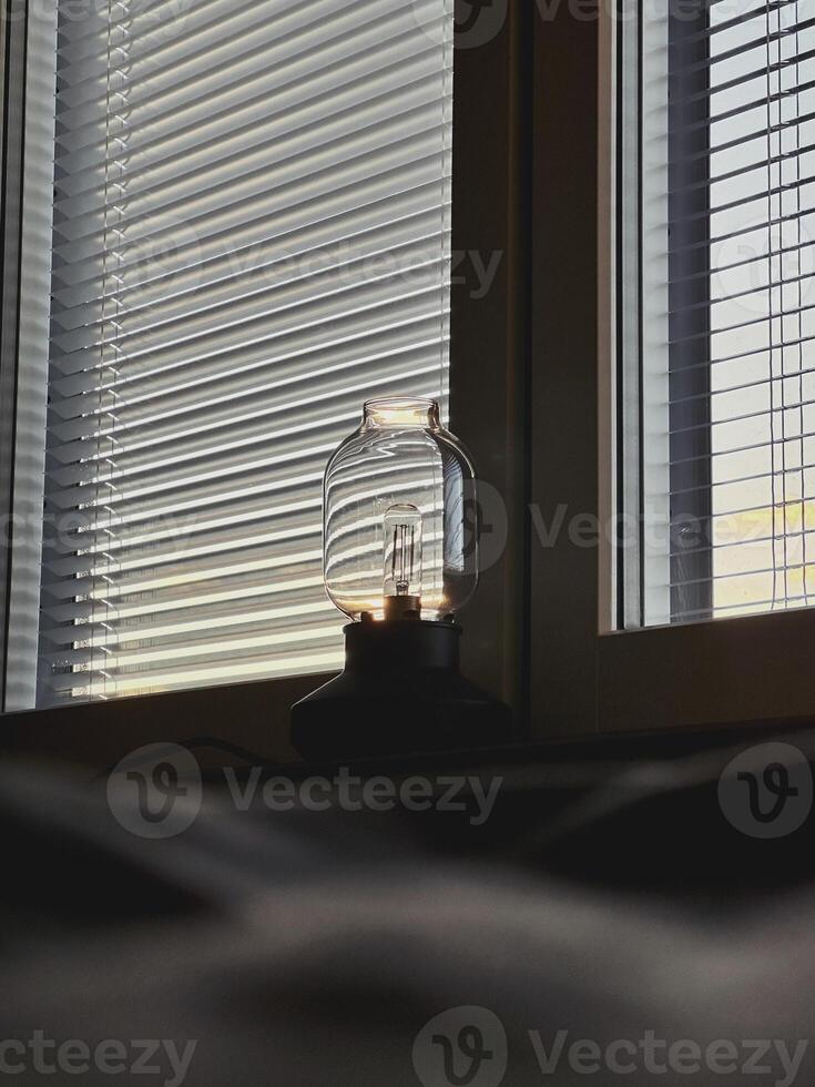 The lamp on the windowsill in front of the window with jalousie, the sunset or sun rise light photo