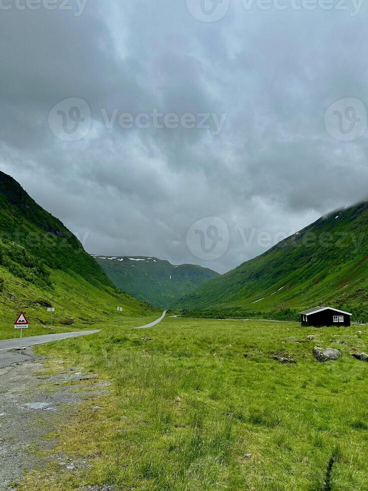 The brown Norwegian national hut Hitta in Norway between the green summer mountains, the road and the road sign go between the mountains photo