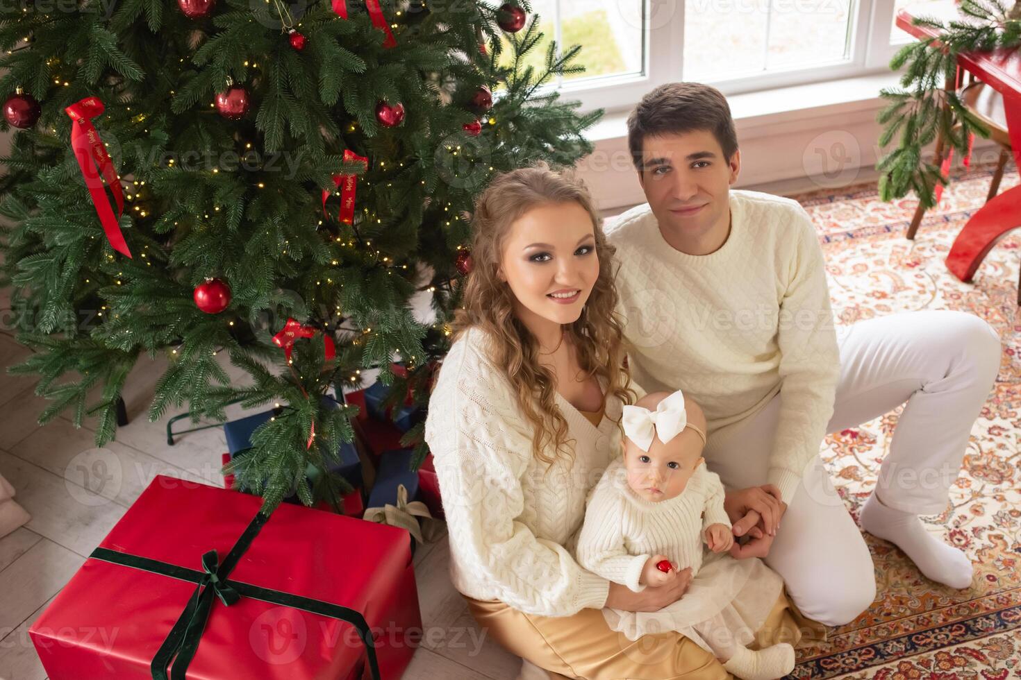 a beautiful family with a little daughter in their arms sits on the floor near a beautiful Christmas tree. happy family concept. parents play with their daughter in a bright room photo
