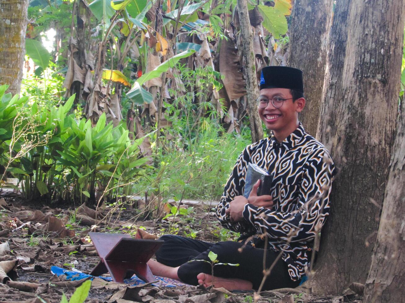 An Asian Muslim man is sitting and reading the Quran. The peace in the middle of forest makes it an energetic atmosphere of faith, traditional vibes photo