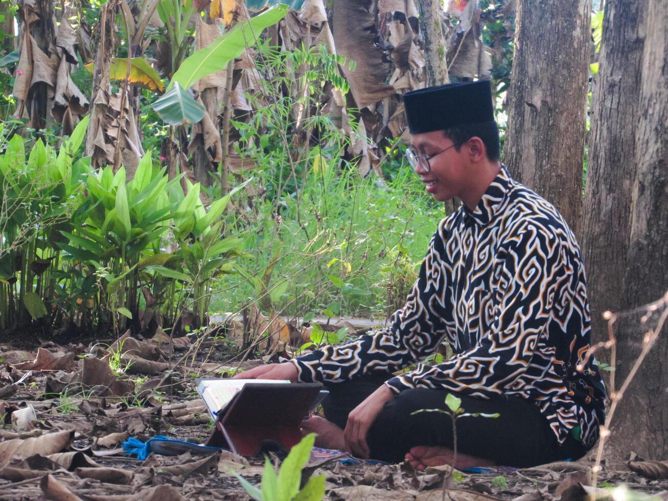 An Asian Muslim man is sitting and reading the Quran. The peace in the middle of forest makes it an energetic atmosphere of faith, traditional vibes photo