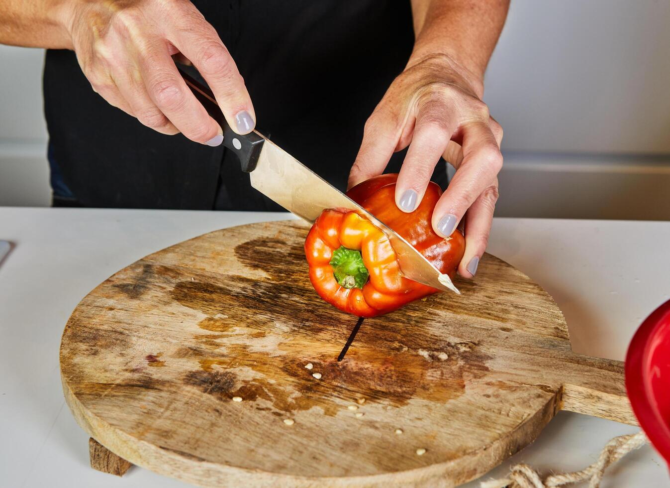 Close-up of hands slicing a red bell pepper on a wooden cutting board, showcasing cooking preparation and fresh ingredients. photo