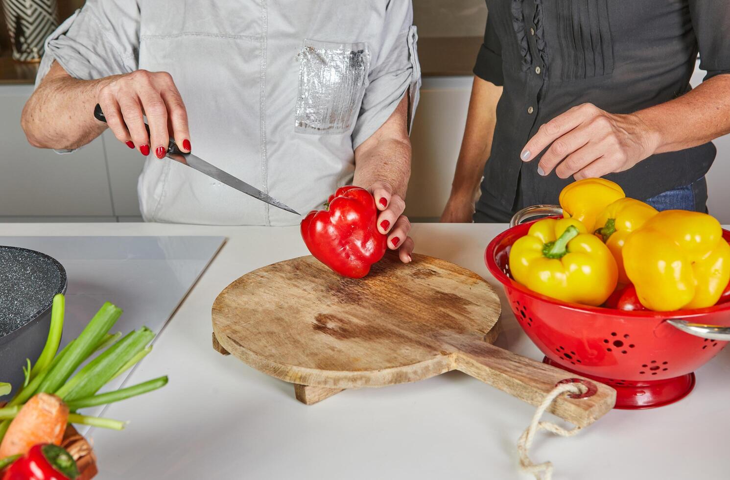 Close-up of hands slicing a red bell pepper on a wooden cutting board, showcasing cooking preparation and fresh ingredients. photo