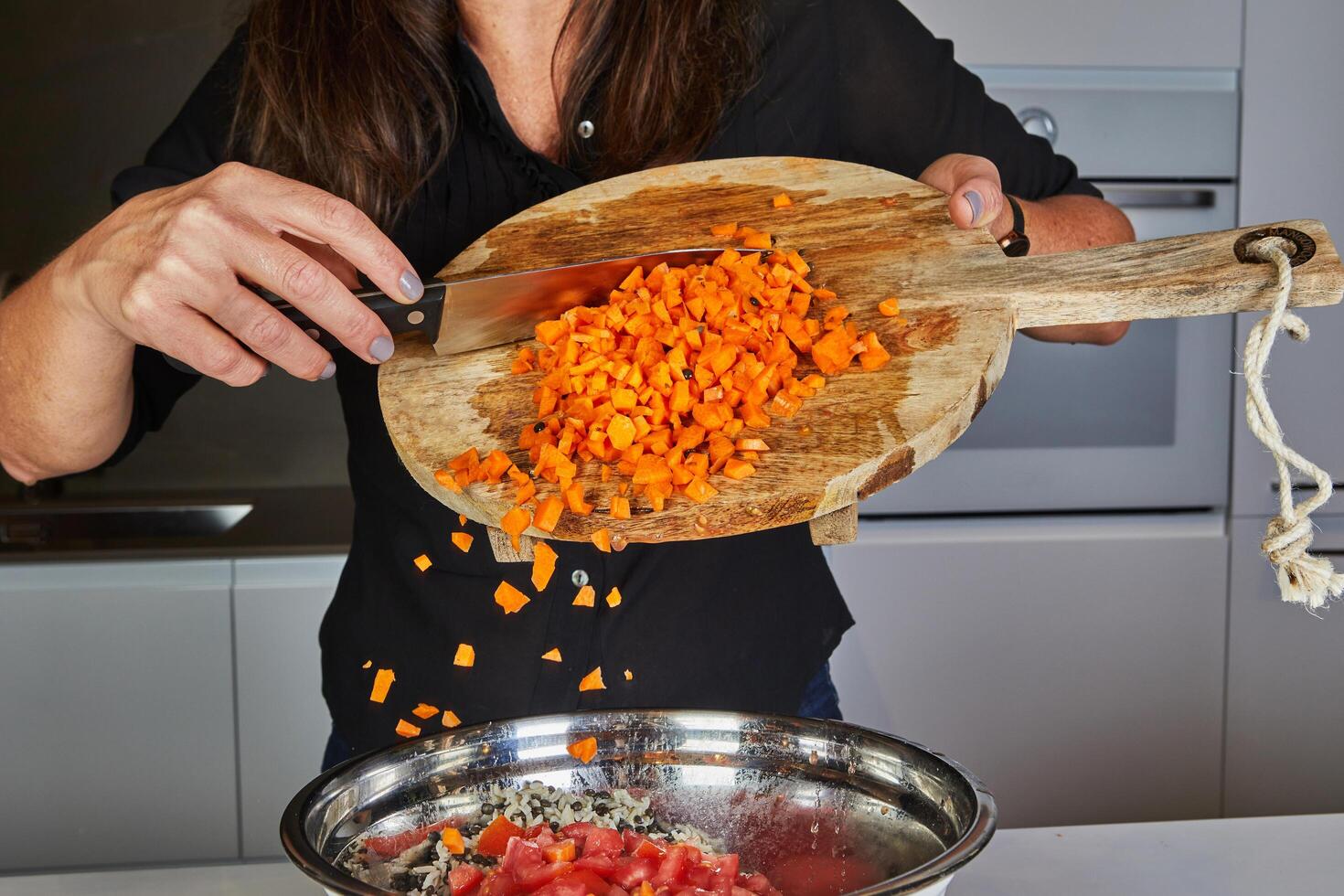 Close-up of hands using a knife to throw fresh carrots from a wooden cutting board into a pan in the kitchen photo