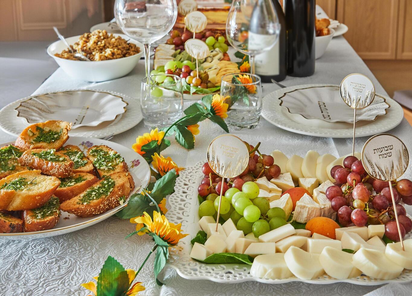 An elegant Shavuot holiday table with wine, cheese, fruit and holiday decorations, ready for a traditional Jewish holiday meal. Happy Shavuot inscriptions in Hebrew. photo