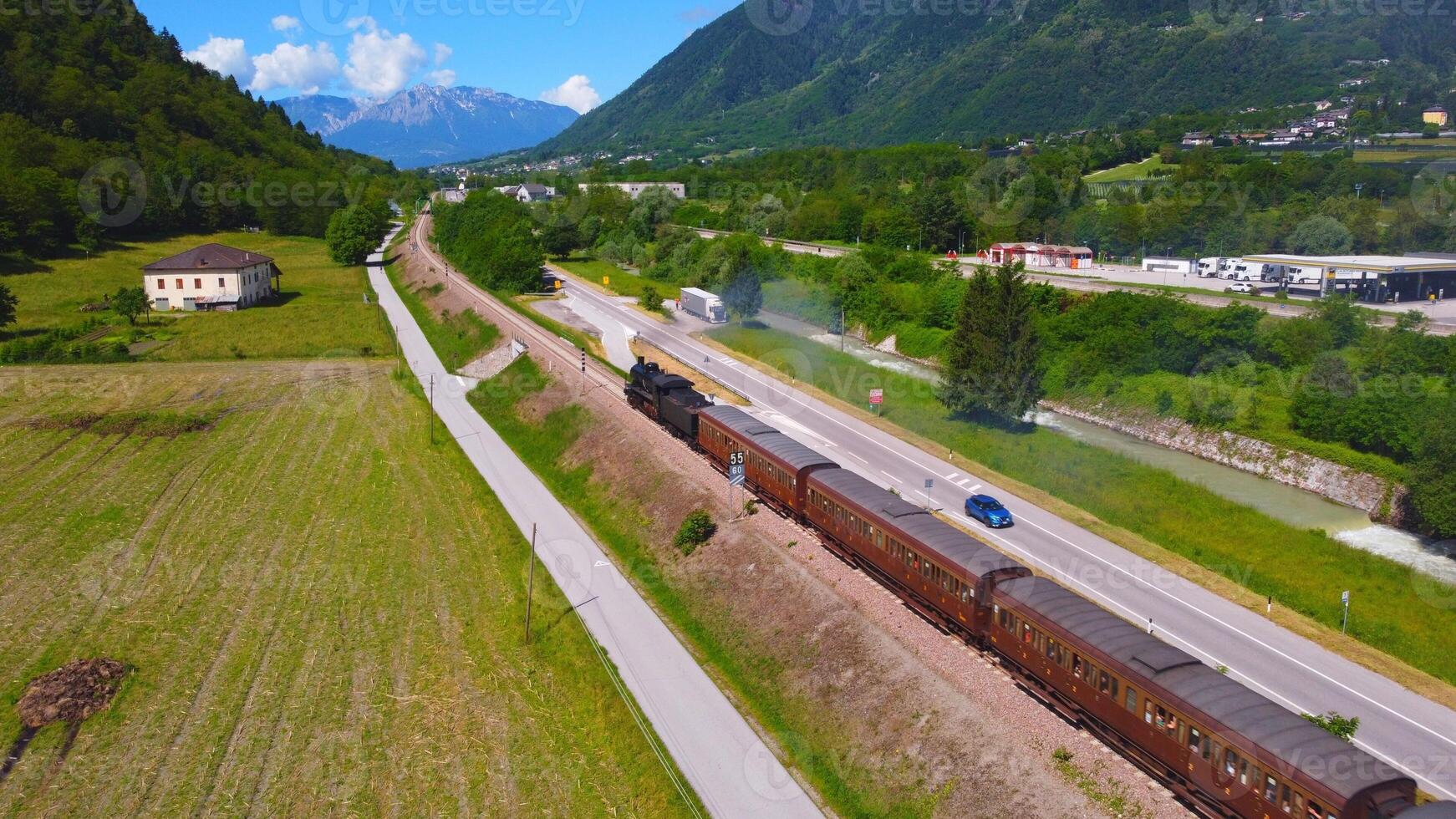 Steam train immersed in the Trentino landscape. old technology that recalls the transport and times of the past, a dive into the past. Romantic of the locomotive with carriages made with a drone photo