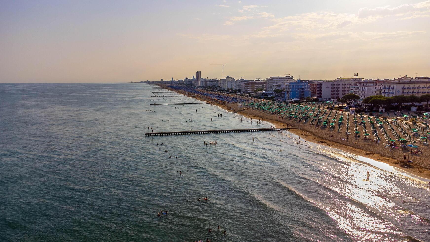 Aerial view of Jesolo beach, near Venice in Italy, coast with sunset. Adriatic Sea in the Mediterranean with beaches full of tourists on holiday and traveling in summer. Top view of umbrellas, hotels. photo