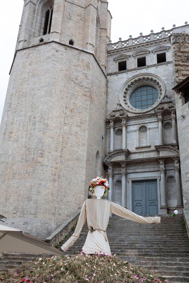 Large mannequin wearing floral crown standing on stone steps in front of church photo