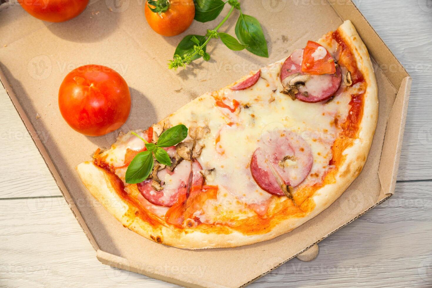 cooked pizza with salami and sausage in a box on a wooden table photo