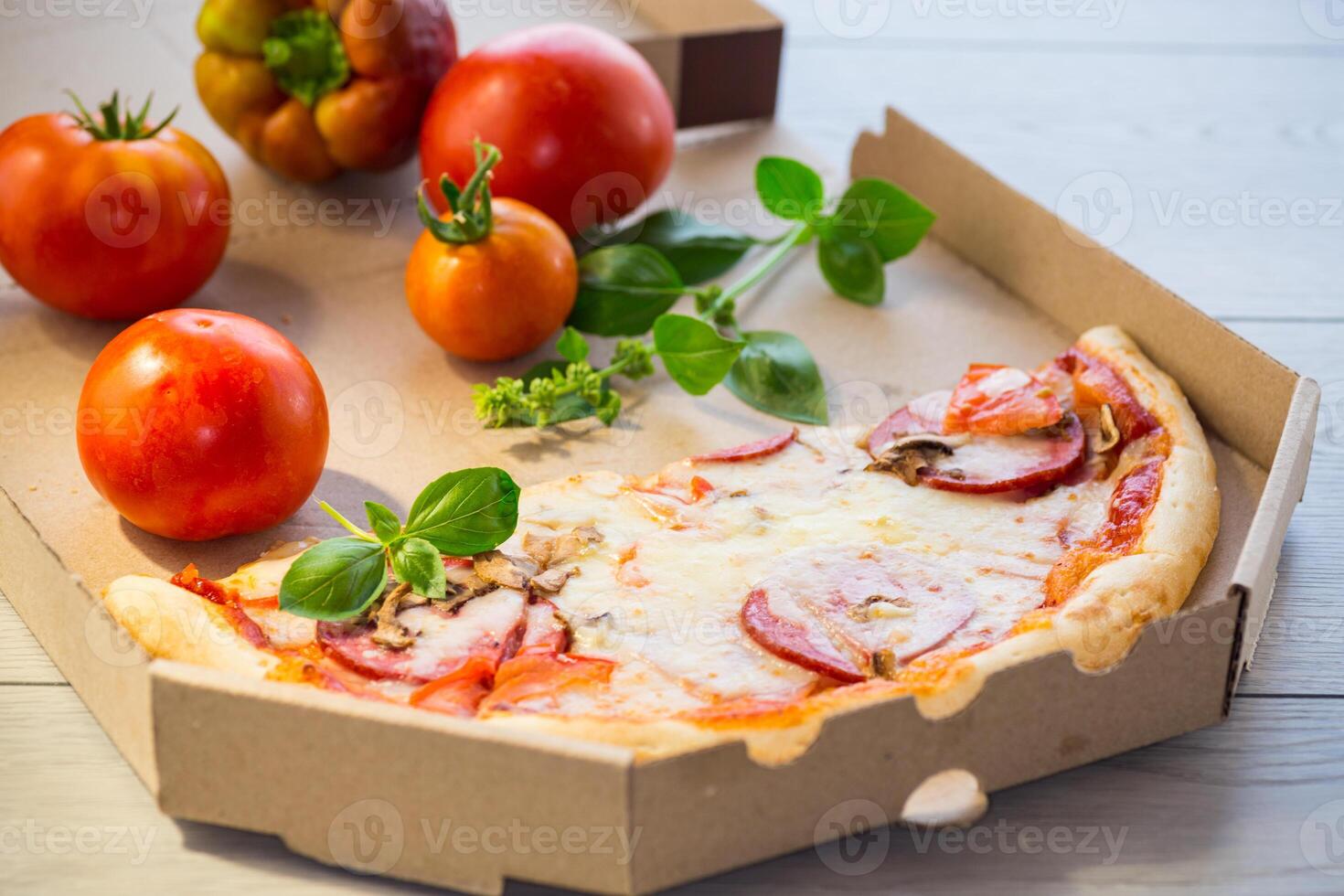 cooked pizza with salami and sausage in a box on a wooden table photo