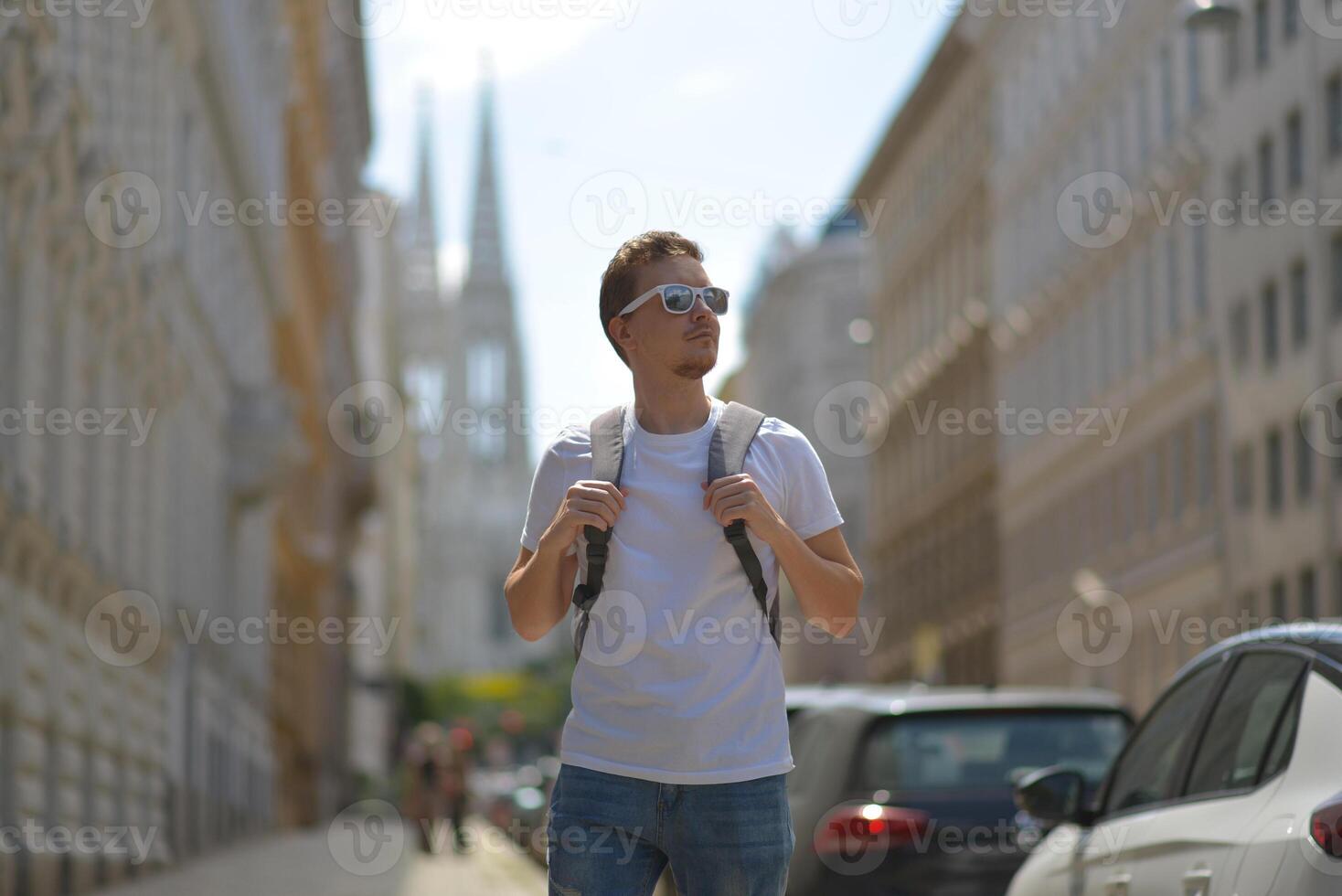 A man wearing white sunglasses and gray backpack on the street in Vienna on a hot sunny summer day. Tourism and sightseeing concept photo