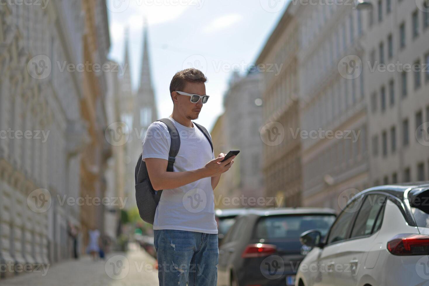 A man using smartphone wearing white sunglasses and gray backpack on the street in Vienna on a hot sunny summer day. Tourism and sightseeing concept photo