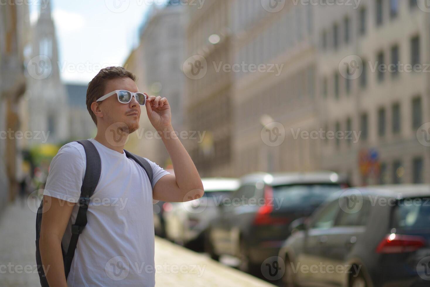 A man wearing white sunglasses and gray backpack on the street in Vienna on a hot sunny summer day. Tourism and sightseeing concept photo