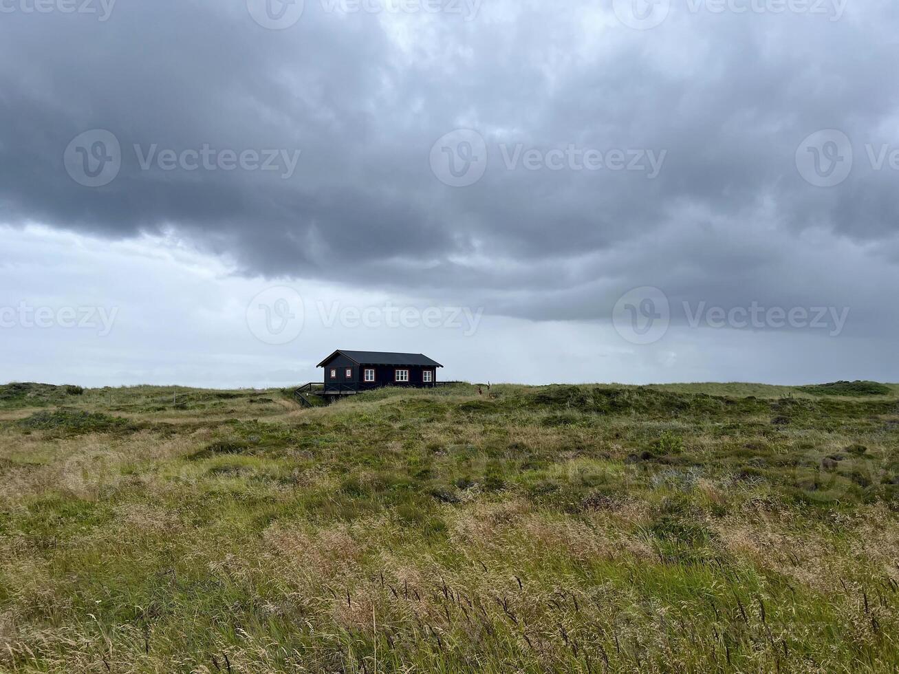 A lonely picturesque house in Danish style on a meadow under the dark cloudy sky before rain, Skagen, on the way to the cape Grenen photo