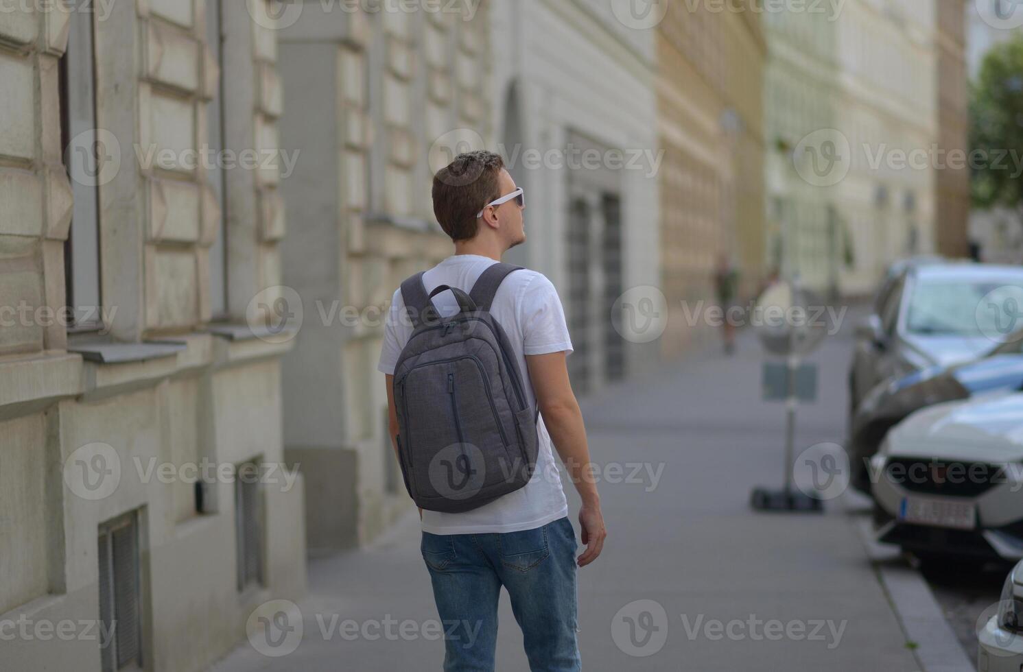 A man wearing white sunglasses and gray backpack on the street in Vienna on a hot sunny summer day. Tourism and sightseeing concept photo