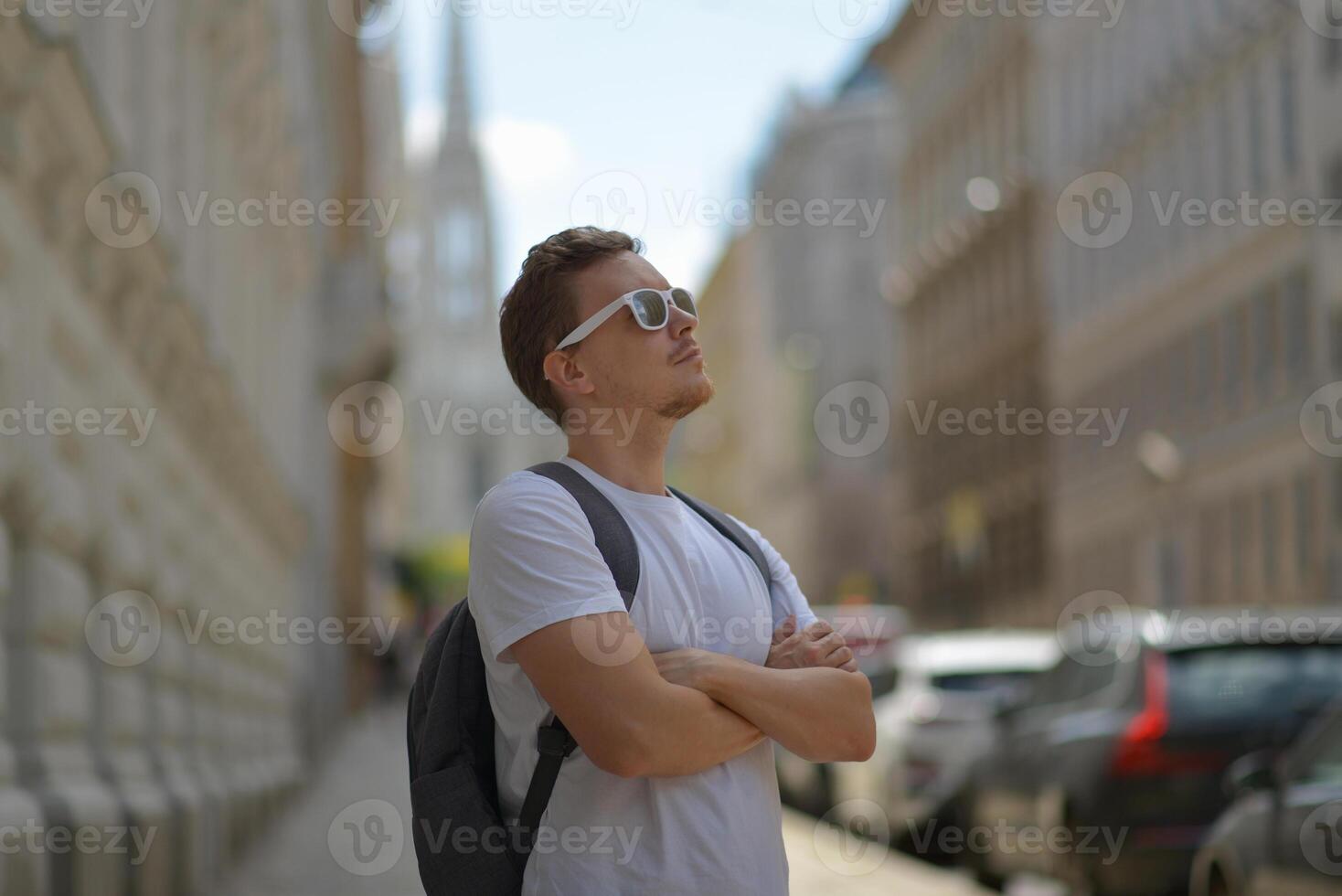 A man wearing white sunglasses and gray backpack on the street in Vienna on a hot sunny summer day. Tourism and sightseeing concept photo