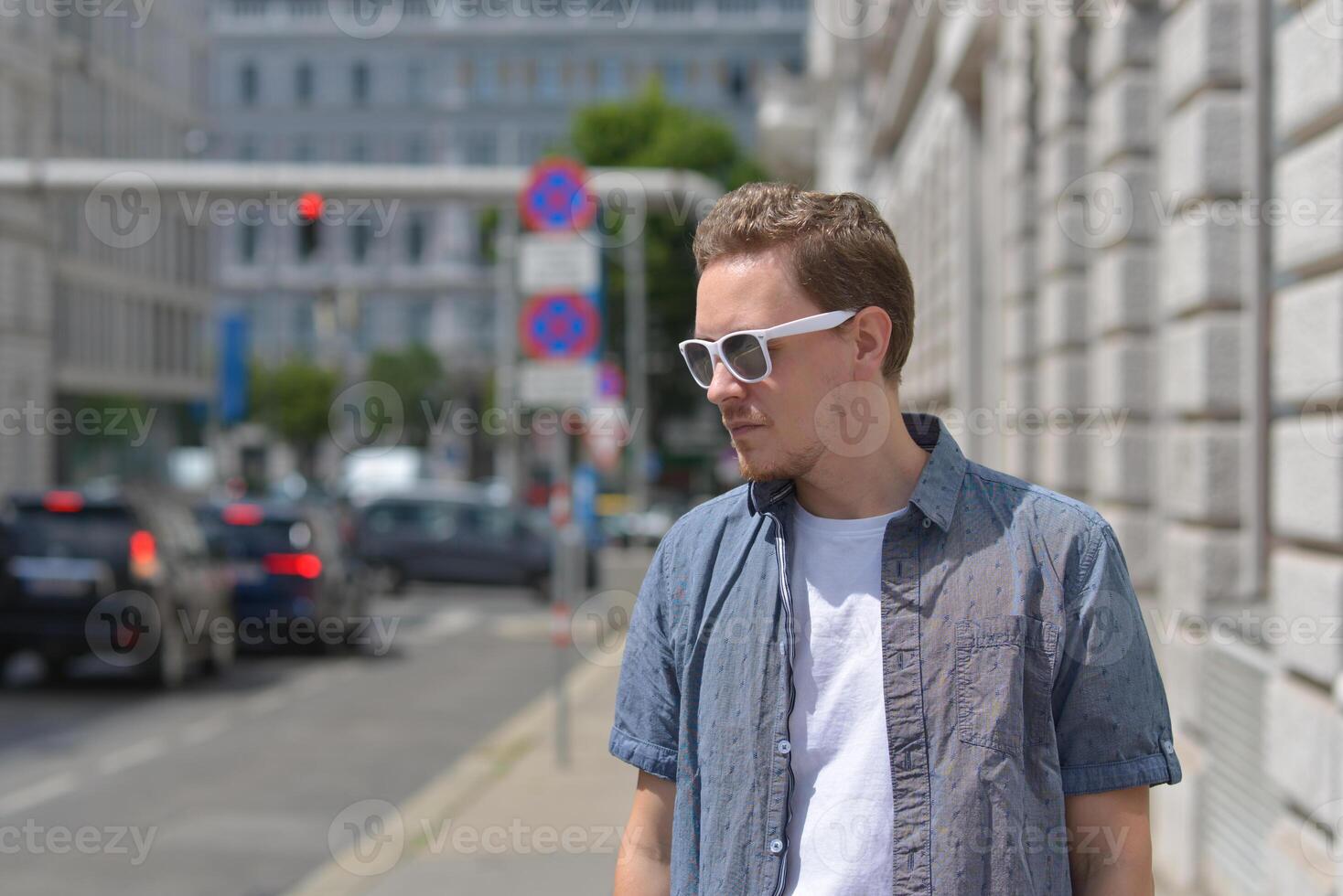 A man wearing sunglasses on the street in Vienna at the background of traffic jam. The concept of hot sunny weather in the city. A man suffers from the heat photo