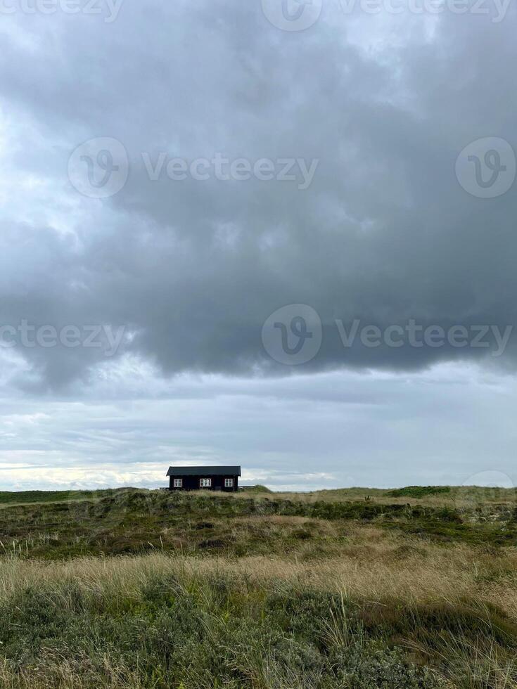 A lonely picturesque house in Danish style on a meadow under the dark cloudy sky before rain, Skagen, on the way to the cape Grenen photo